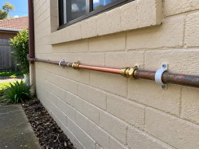 Repaired copper water pipe along a brick exterior wall beneath a window in Glenwood