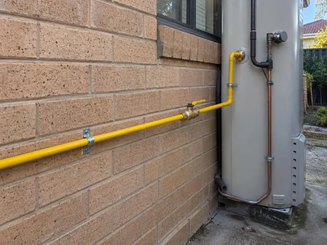 Yellow gas pipe and fittings beside an outdoor water heater on a brick wall in Glenwood